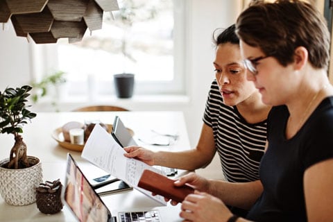 Two women reviewing their finances on paper and a laptop.